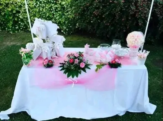 Tavolo allestito con confetti, sacchetti rosa, bouquet centrale di rose e ortensie, decorazioni per cerimonia di battesimo.