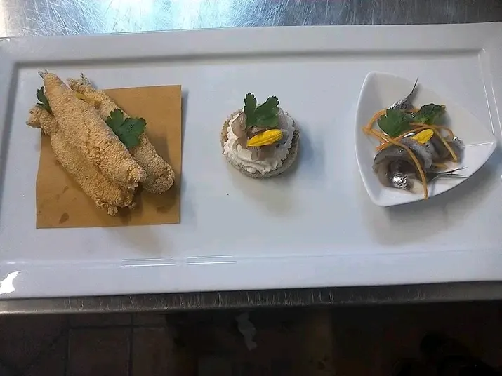 Vassoio in ceramica bianca con tre piatti: filetti di pesce fritto, tartare con lamelle d'arancia, antipasto di pesce con prezzemolo.
